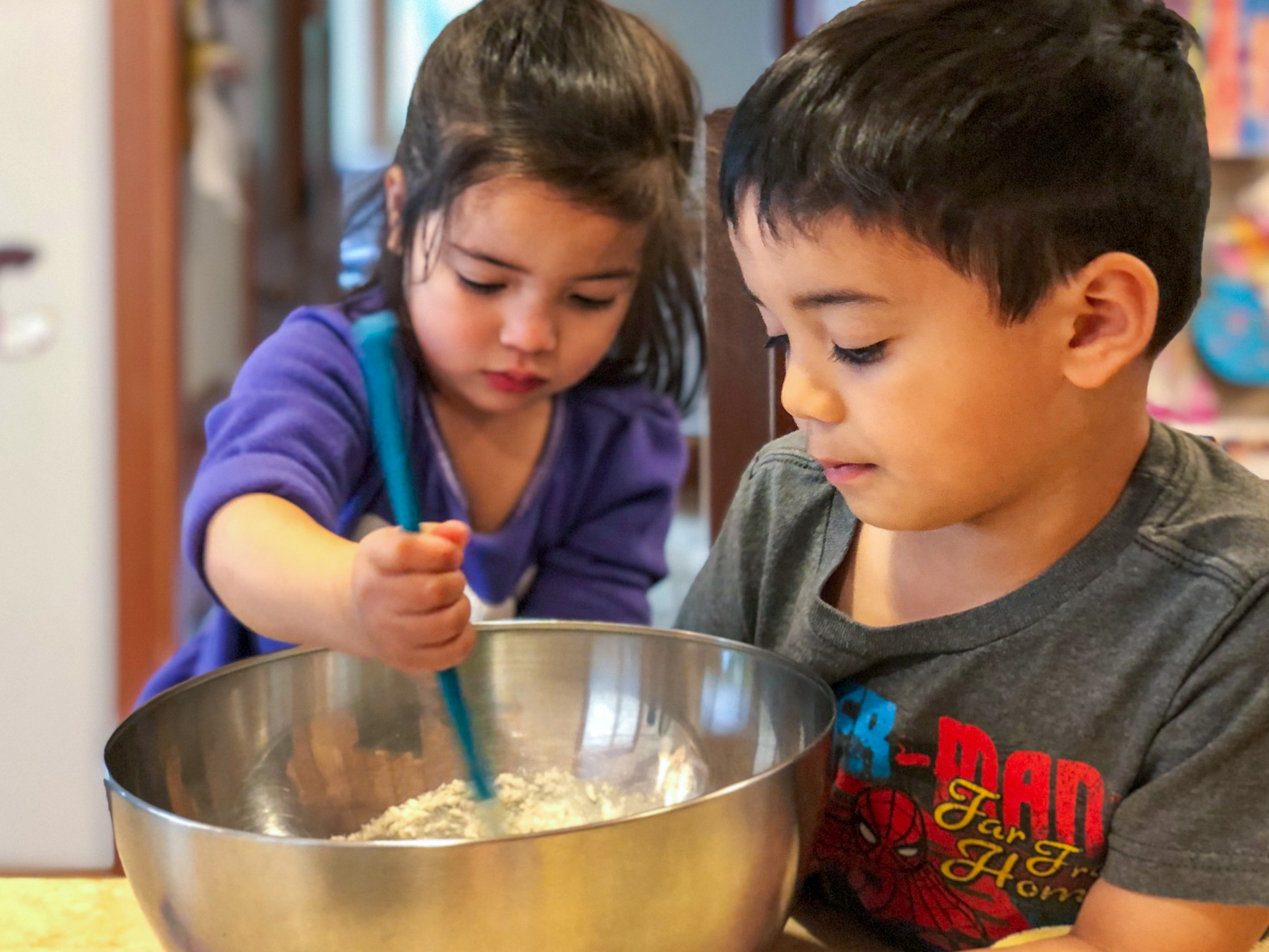 Two young children work together to stir a bowl of food