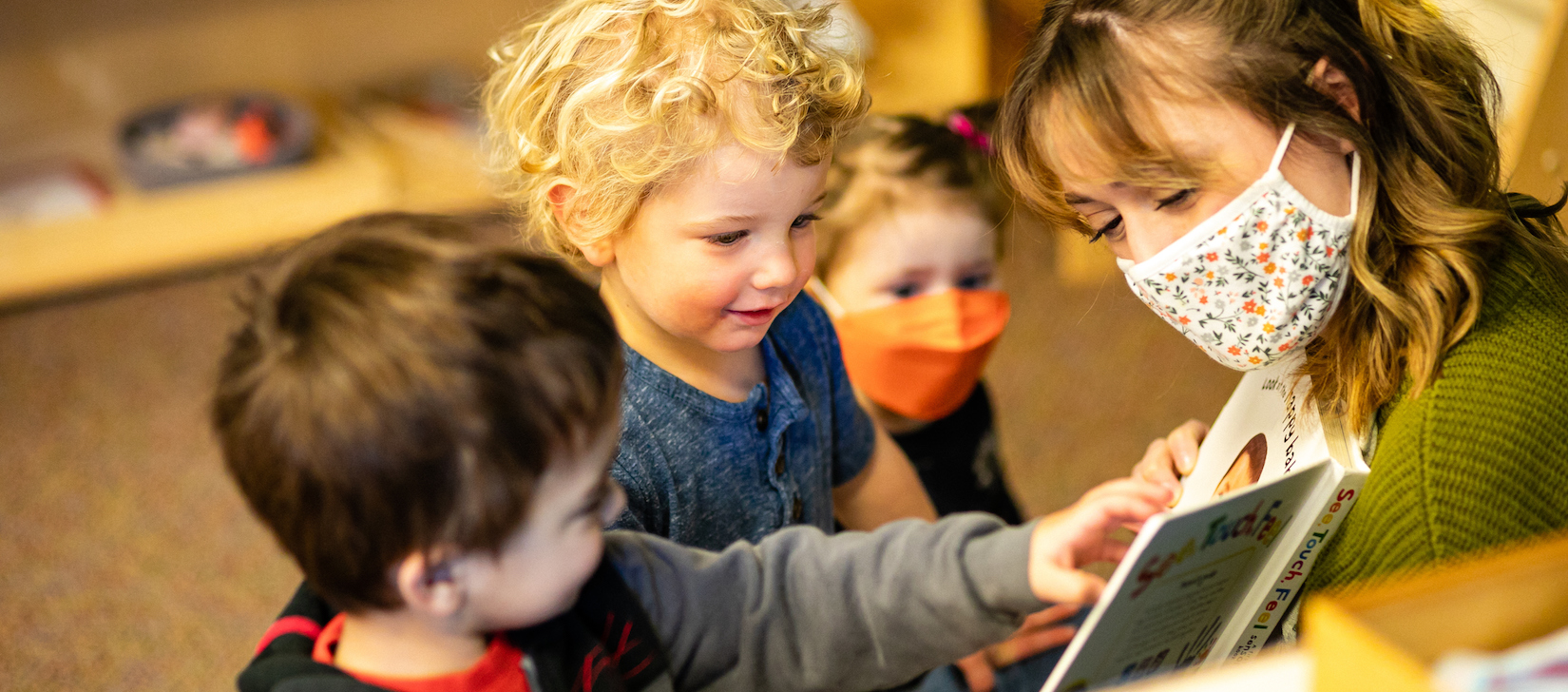 A photo of a teacher showing a book to three students in a classroom